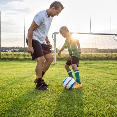 Coach and young football player on football ground at sunset Coach and young football player on football ground at sunset