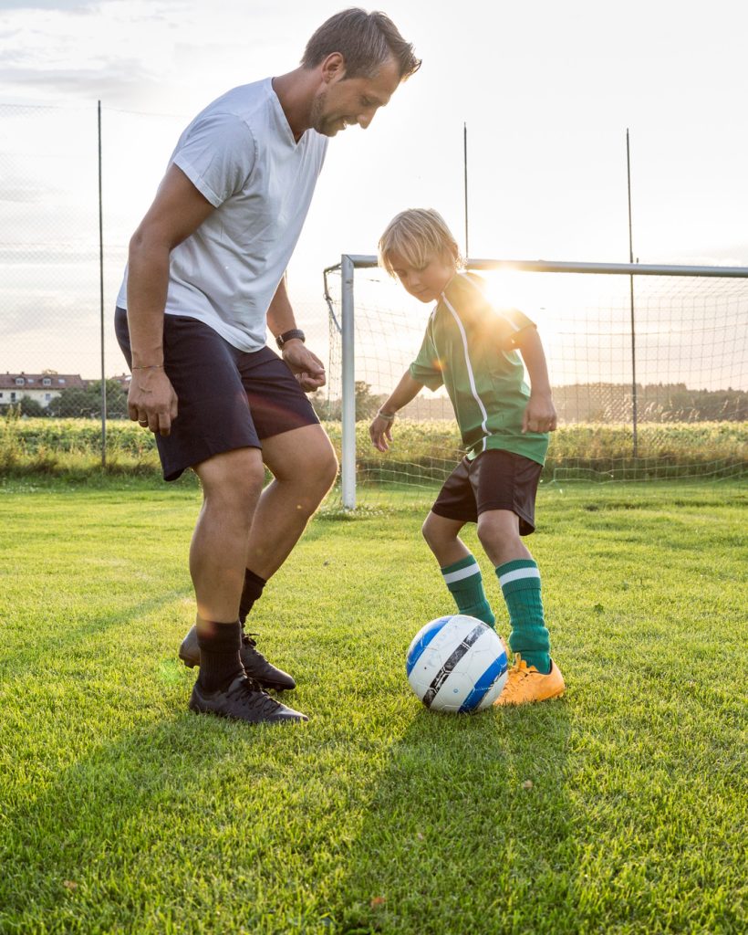 Coach and young football player on football ground at sunset
