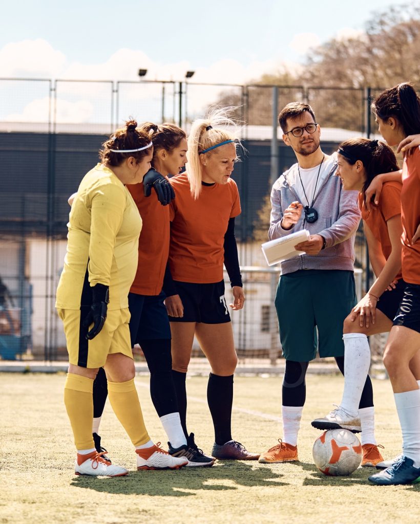 Soccer coach planning game strategy with female team on playing field.